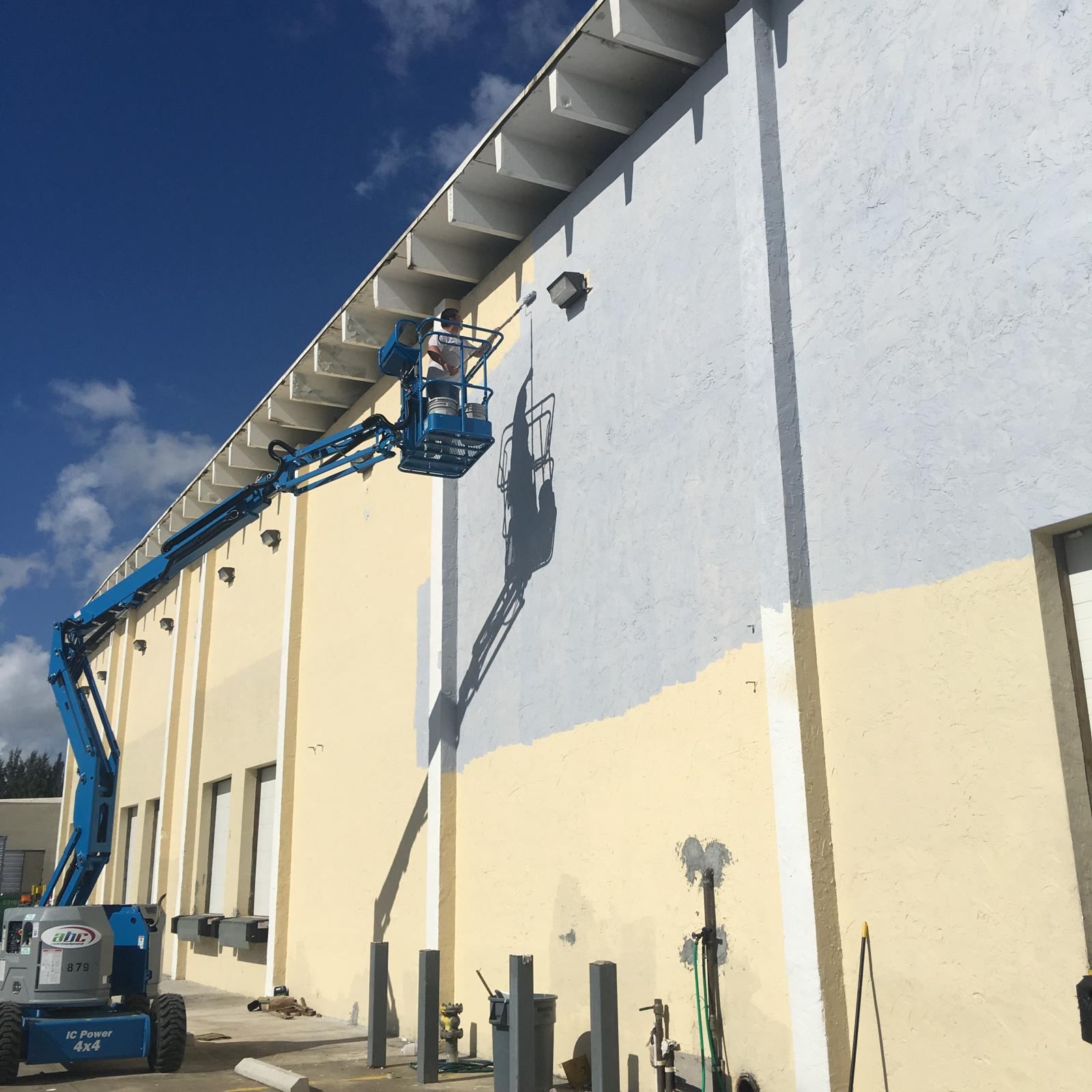 Painter on a boom lift painting a warehouse wall